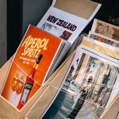 Assorted vintage posters in a wooden stand featuring travel and beverage themes.